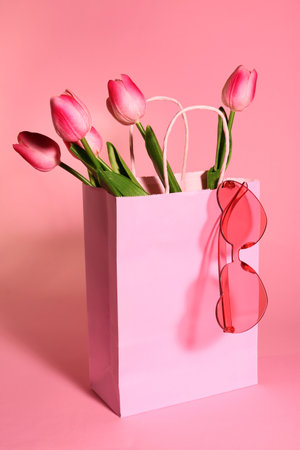Shopping bag with beautiful tulips and stylish sunglasses on pink backgroundの写真素材