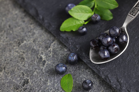 Spoon with tasty fresh bilberries on dark gray table, closeup. Space for textの写真素材