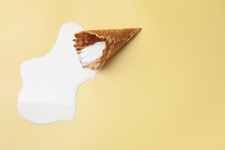 Melted ice cream and wafer cone on beige background, top view. Space for textの写真素材