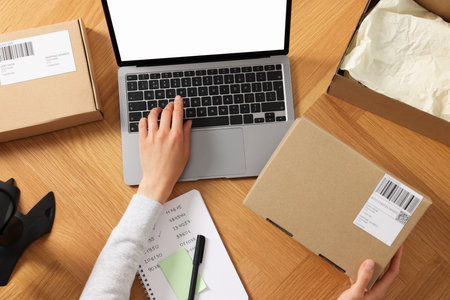 Woman with laptop and parcel working at wooden table, top view. Online storeの写真素材