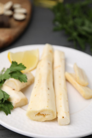 Cut raw salsify roots with parsley and lemon on white plate, closeup