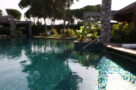 Blurred view of swimming pool, metal rail and tropical plants at luxury resort