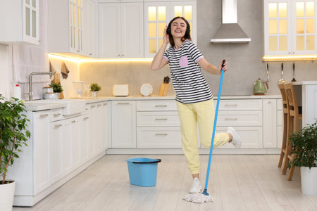 Enjoying cleaning. Woman in headphones listening music and mopping in kitchen