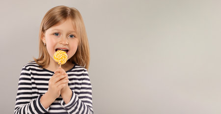Portrait of cute girl licking lollipop on light grey background, space for textの写真素材