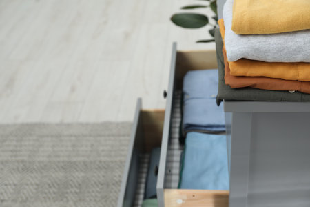 Sorting and organizing. Chest of drawers with different folded clothes indoors, space for text