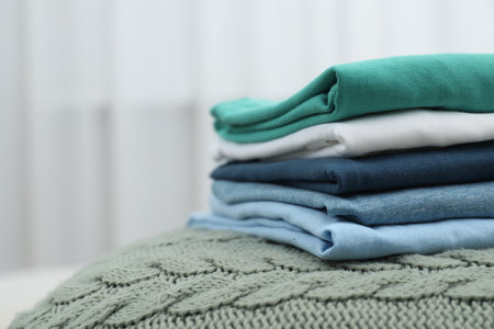 Sorting and organizing. Stack of different folded clothes on bed indoors, space for text