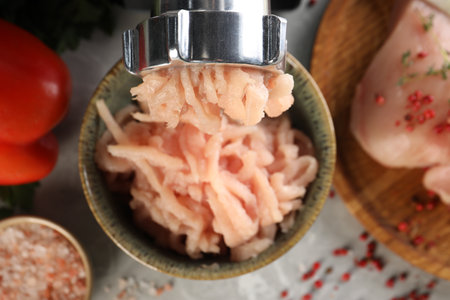 Electric meat grinder with chicken mince and products on gray table indoors, flat lay