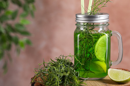Mason jar of homemade refreshing tarragon drink with lemon slices and sprigs on wooden stump, closeup. Space for textの写真素材