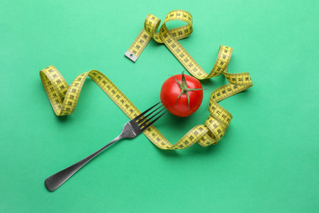 Tomato, fork and measuring tape on green background, flat lay. Diet conceptの写真素材