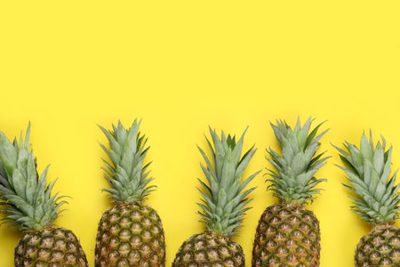 Whole ripe pineapples on yellow background, flat lay. Space for textの写真素材