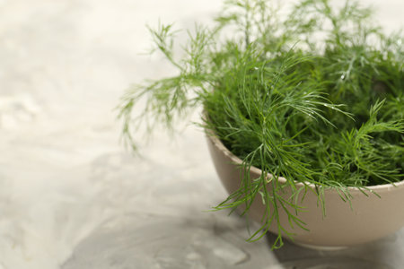 Bowl of fresh green dill on light gray table, closeup. Space for text