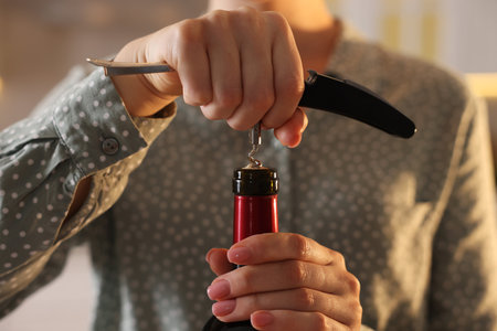 Woman opening wine bottle with corkscrew indoors, closeup