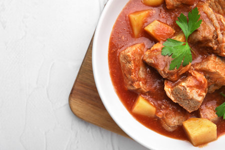 Delicious goulash in bowl on white textured table, top view. Space for textの写真素材
