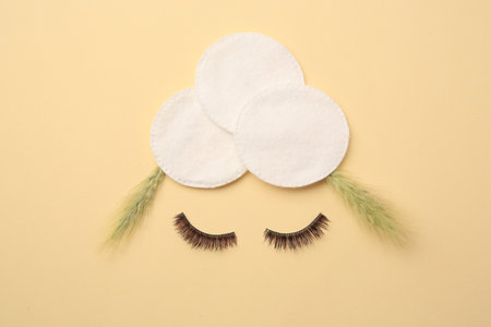 Flat lay composition with cotton pads, spikelets and false eyelashes on yellow background. Makeup...