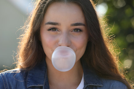 Beautiful young woman blowing bubble gum outdoorsの写真素材