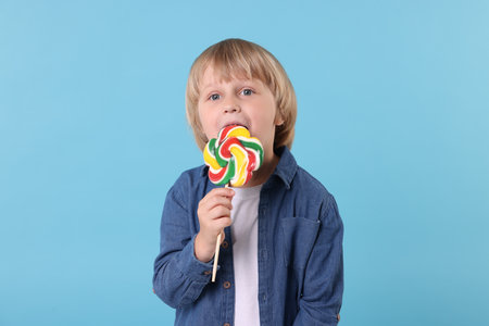 Cute little boy licking colorful lollipop swirl on light blue backgroundの写真素材