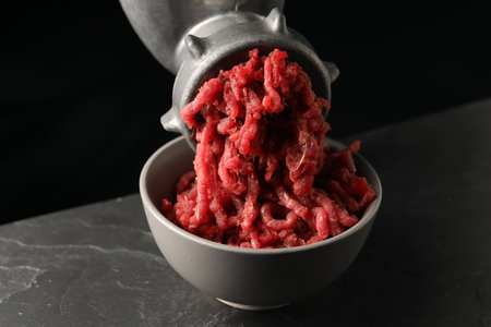 Metal meat grinder with beef mince on dark textured table against black background, closeupの写真素材