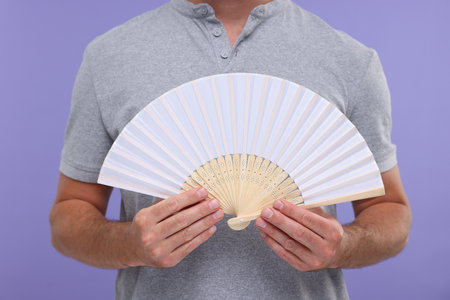 Man holding hand fan on purple background, closeupの写真素材