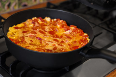 Tasty fried eggs with tomatoes in frying pan on stove, closeupの写真素材