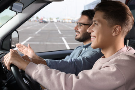 Driving school. Happy student during lesson with driving instructor in car at parking lotの写真素材