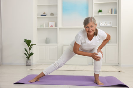 Happy senior woman practicing yoga on mat at homeの写真素材