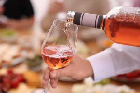 Man pouring rose wine from bottle into glass indoors, closeupの写真素材