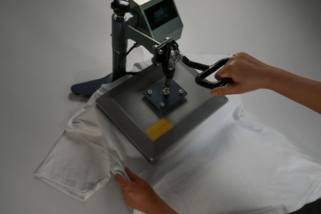 Printing logo. Woman with t-shirt using heat press at white table, above viewの写真素材