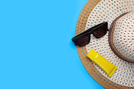 Straw hat, sunscreen and sunglasses on light blue background, flat lay and space for text. Beach...
