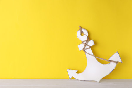 Anchor with hemp rope on white wooden table near yellow wall, space for textの写真素材
