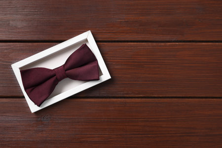 Stylish burgundy bow tie in box on wooden table, top view. Space for textの写真素材