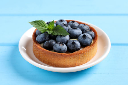 Tartlet with fresh blueberries on light blue wooden table, closeup. Delicious dessertの写真素材