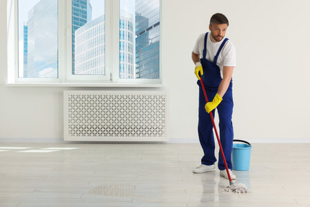 Man in uniform cleaning floor with mop indoors. Space for textの写真素材