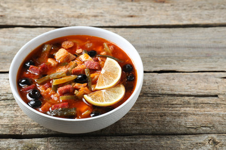 Meat Solyanka soup with sausages, olives and vegetables in bowl on wooden table. Space for textの写真素材