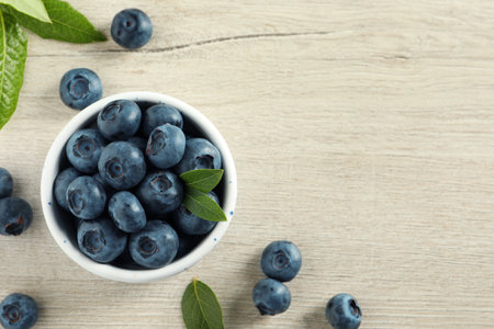 Bowl of fresh tasty blueberries with leaves on white wooden table, flat lay. Space for textの写真素材