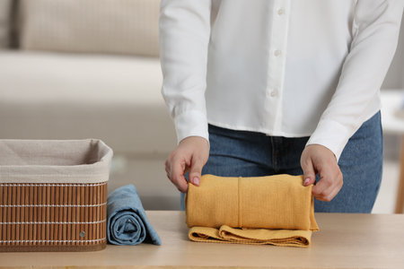 Woman rolling shirt at table indoors, closeup. Organizing clothes