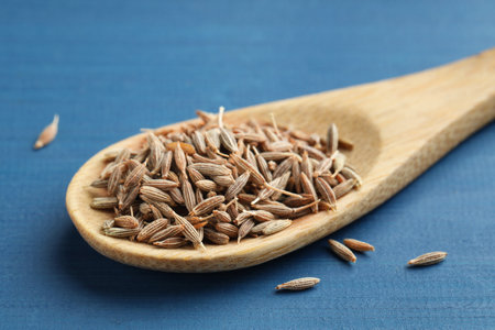 Spoon with caraway seeds on blue wooden table, closeup