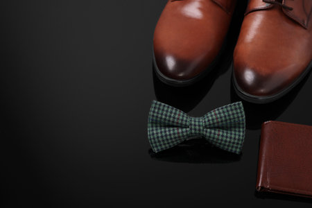 Stylish green checkered bow tie, wallet and shoes on black surface, space for textの写真素材