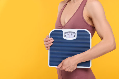 Slim woman holding scales on yellow background, closeup and space for text. Weight lossの写真素材