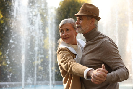 Affectionate senior couple dancing together near fountain outdoors, space for textの写真素材