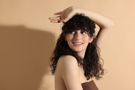 Portrait of beautiful young woman in sunlight on beige background, space for text