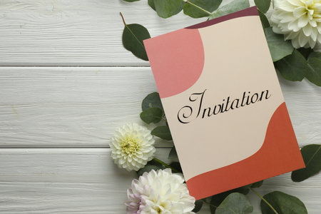 Card with word Invitation and beautiful flowers on white wooden background, flat lay. Space for textの写真素材