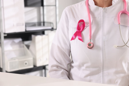 Doctor with stethoscope and pink ribbon at white desk indoors, closeup. Breast cancer awarenessの写真素材