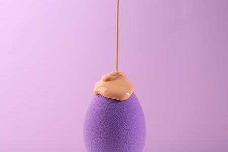 Pouring skin foundation onto makeup sponge on violet background, closeupの写真素材