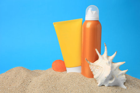 Sand with sunscreens and seashells against blue background, space for text. Sun protection careの写真素材