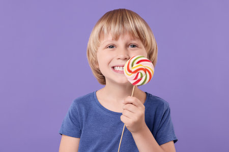 Happy little boy with colorful lollipop swirl on violet backgroundの写真素材