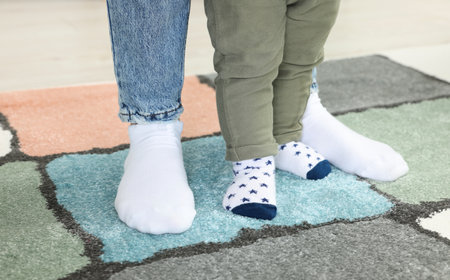 Mother supporting her son while he learns to walk on carpet indoors, closeup