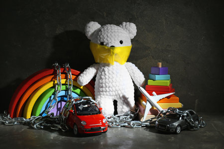 Stop child abuse. Crochet bear with taped mouth, chain and toys in dark roomの写真素材