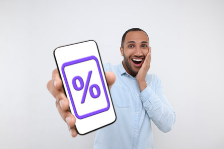 Discount, offer, sale. Emotional man showing mobile phone with percent sign on screen, white backgroundの写真素材