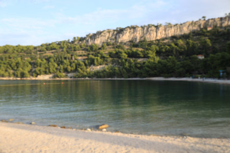Blurred view of green trees and mountains near tranquil sea