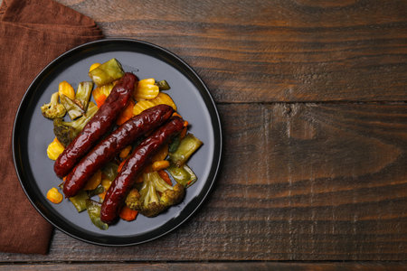 Delicious smoked sausages and baked vegetables on wooden table, top view. Space for textの写真素材